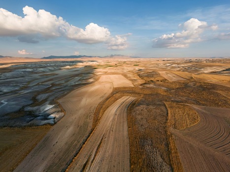 Aerial view of vast agricultural fields with golden and brown harvested crops rolling terrain and shadows cast under a bright sky in the rural landscape of Sivrihisar Eskisehir Turkey. Aerial view of vast agricultural fields with golden and brown harvested crops rolling terrain and shadows cast under a bright sky in the rural landscape of Sivrihisar Eskisehir Turkey.