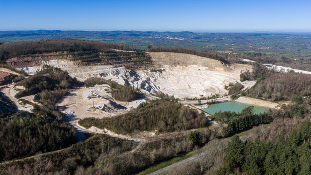 Aerial view of the stark white quarry contrasting against the lush green forest and a serene blue lake &Eacute;chassi&egrave;res Auvergne Rh&ocirc;ne Alpes France.