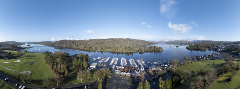 Aerial view of boats docked at the marina reflecting the clear sky nestled between verdant hills and the calm lake Bowness on Windermere England United Kingdom. Aerial view of boats docked at the marina reflecting the clear sky nestled between verdant hills and the calm lake Bowness on Windermere England United Kingdom.