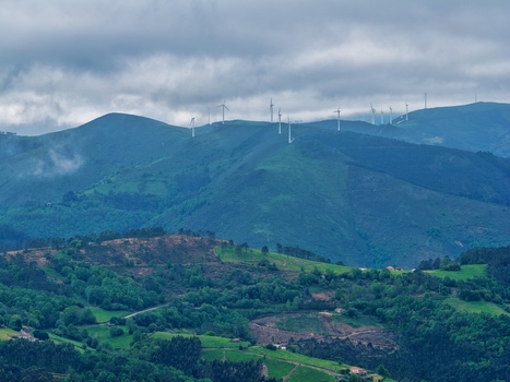 Aerial view of wind turbines standing on lush green mountain ridges under a dramatic cloudy sky in Cudillero Asturias Spain.