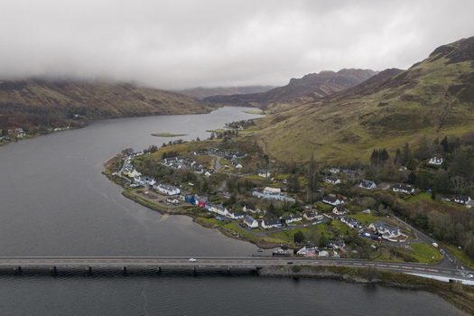 Aerial view of the village of Dornie with colorful houses along the waterfront and the bridge crossing Loch Long under a misty sky in Dornie Scotland United Kingdom.