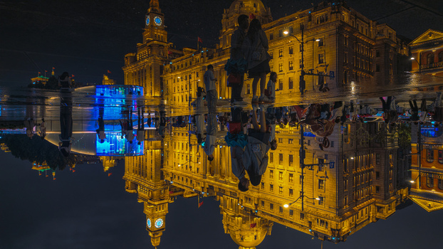 View of The Bund illuminated at night with a clear reflection in a puddle on the ground and people standing nearby in Shanghai Shanghai China.