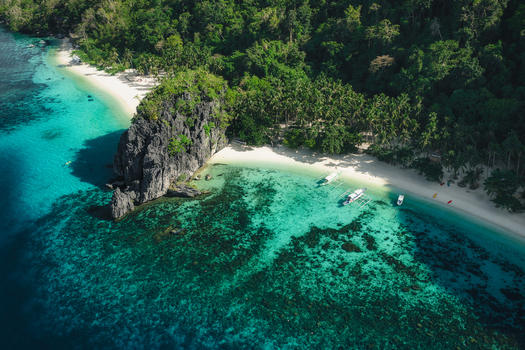 Aerial view of Papaya Beach with turquoise waters coral reefs limestone cliffs and outrigger boats moored on the white sand in El Nido Mimaropa Philippines. Aerial view of Papaya Beach with turquoise waters coral reefs limestone cliffs and outrigger boats moored on the white sand in El Nido Mimaropa Philippines.