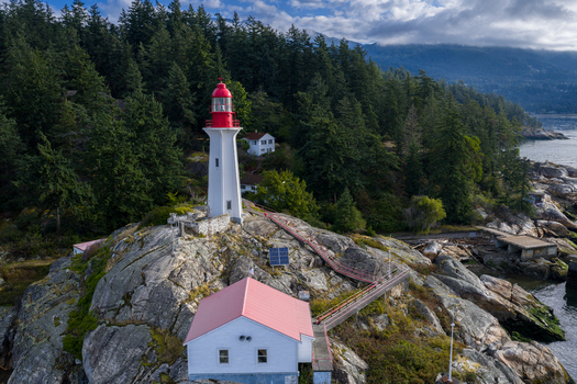 Aerial view of Point Atkinson Lighthouse Federal Heritage Building situated on a rocky coastline surrounded by dense evergreen forest in West Vancouver British Columbia Canada.
