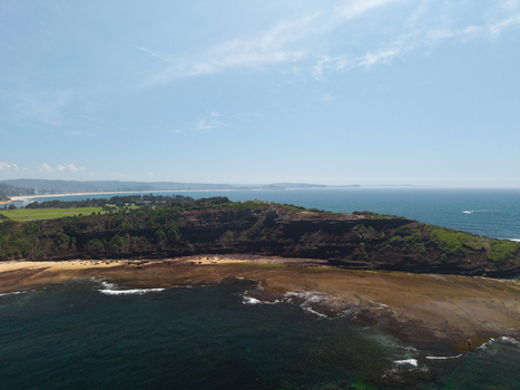 Aerial view of Long Reef Headland featuring rugged cliffs rocky shorelines and lush vegetation overlooking the Pacific Ocean in Collaroy New South Wales Australia.