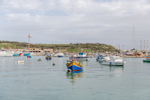 View of vibrant colorful boats bobbing gently on the tranquil turquoise waters of the harbor against a backdrop of buildings Marsaxlokk Malta. View of vibrant colorful boats bobbing gently on the tranquil turquoise waters of the harbor against a backdrop of buildings Marsaxlokk Malta.