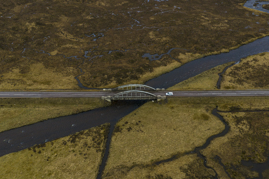 Aerial view of River Etive Bridge crossing the dark river amidst the vast moorland of the Scottish Highlands with a lone white car Ballachulish Scotland United Kingdom. Aerial view of River Etive Bridge crossing the dark river amidst the vast moorland of the Scottish Highlands with a lone white car Ballachulish Scotland United Kingdom.