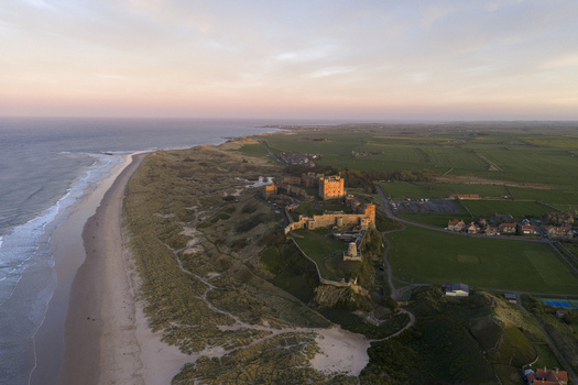 Aerial view of Bamburgh Castle on a rocky outcrop overlooking the North Sea and sandy dunes under a sunset sky Bamburgh England United Kingdom. Aerial view of Bamburgh Castle on a rocky outcrop overlooking the North Sea and sandy dunes under a sunset sky Bamburgh England United Kingdom.
