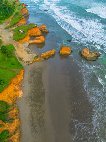 Aerial view of rugged orange cliffs meeting the dark sand beach and turquoise waves of the ocean in Bali Indonesia. Aerial view of rugged orange cliffs meeting the dark sand beach and turquoise waves of the ocean in Bali Indonesia.