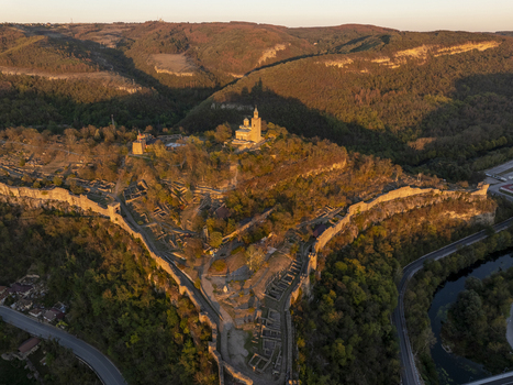 Aerial view of Tsarevets Fortress illuminated by golden hour light featuring historic stone walls ruins and the central church atop the hill in Veliko Tarnovo Veliko Tarnovo Bulgaria. Aerial view of Tsarevets Fortress illuminated by golden hour light featuring historic stone walls ruins and the central church atop the hill in Veliko Tarnovo Veliko Tarnovo Bulgaria.