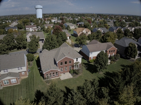 Aerial view of a residential neighborhood featuring suburban houses manicured lawns mature trees and a distant water tower under a clear blue sky in Mason Ohio United States.