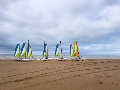View of several catamarans with colorful sails parked on the sandy beach under a cloudy sky in Saint Jean de Monts Pays de la Loire France.