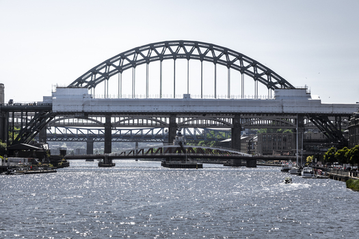 View of the iconic Tyne Bridge spanning the River Tyne with its distinctive green arch framed by the surrounding cityscape and river traffic in Newcastle upon Tyne England United Kingdom. View of the iconic Tyne Bridge spanning the River Tyne with its distinctive green arch framed by the surrounding cityscape and river traffic in Newcastle upon Tyne England United Kingdom.