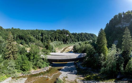 Aerial view of the historic Sodbachbrucke Sense wooden covered bridge spanning the river surrounded by lush green forests and rocky terrain in Heitenried Freiburg Switzerland. Aerial view of the historic Sodbachbrucke Sense wooden covered bridge spanning the river surrounded by lush green forests and rocky terrain in Heitenried Freiburg Switzerland.