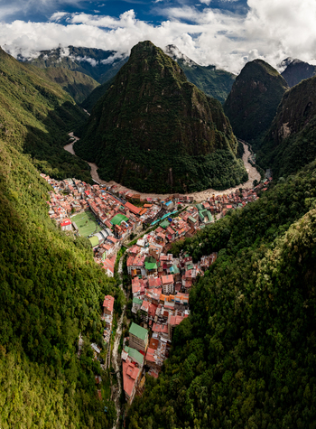Aerial view of the town of Aguas Calientes nestled in a deep valley surrounded by lush green Andean mountains and the winding Urubamba River in Aguas Calientes Cusco Peru.