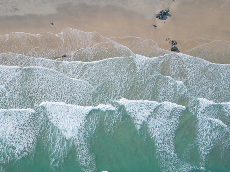 Aerial view of turquoise waves crashing on the sandy shore of Porthmeor Beach with scattered rocks in St Ives Cornwall United Kingdom.