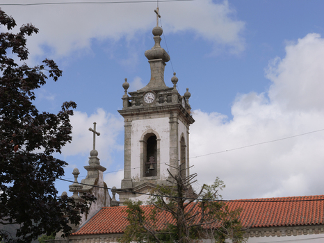 View of the stone bell tower of Igreja de Nossa Senhora da Conceicao da Covilha with a clock and cross against a blue sky in Covilha Castelo Branco Portugal.