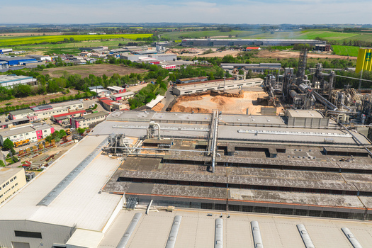 Aerial view of a large industrial factory complex with extensive rooftops processing machinery and storage areas under a clear sky in Jihlava Vysocina Region Czechia.