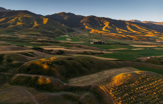 Aerial view of Chon Kemin valley landscape with rolling hills agricultural fields and golden hour sunlight illuminating the mountain slopes in Kaindy Chuy Province Kyrgyzstan.