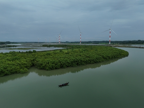 Aerial view of the Khurushkul wind farm with turbines in a lush mangrove landscape and a small boat on the river. Cox s Bazar Chittagong Division Bangladesh. Aerial view of the Khurushkul wind farm with turbines in a lush mangrove landscape and a small boat on the river. Cox s Bazar Chittagong Division Bangladesh.
