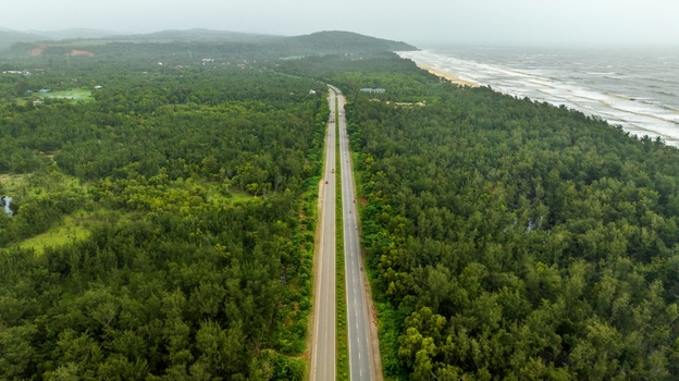 Aerial view of a straight highway stretching through dense green forests along the coastline in Honnavar Karnataka India.