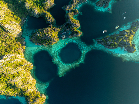 Aerial view of Twin Lagoon featuring dramatic limestone cliffs turquoise and deep blue waters and small boats floating in the tropical landscape of Coron Mimaropa Philippines. Aerial view of Twin Lagoon featuring dramatic limestone cliffs turquoise and deep blue waters and small boats floating in the tropical landscape of Coron Mimaropa Philippines.