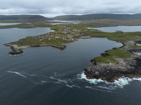 Aerial view of Fugla Ness Lighthouse and the coastal village of Hamnavoe surrounded by rocky cliffs green hills and the sea in Hamnavoe Scotland United Kingdom.