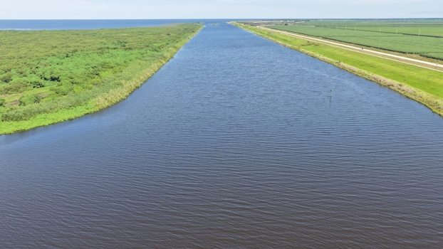 Aerial view of the canal near Lake Okeechobee with lush green vegetation and agricultural fields under a clear blue sky in Pahokee Florida United States.