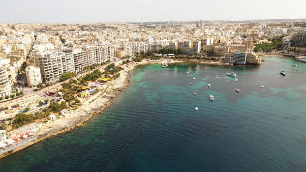 Aerial view of the coastal urban landscape with turquoise waters moored boats and dense residential buildings along the rocky shoreline in Malta. Aerial view of the coastal urban landscape with turquoise waters moored boats and dense residential buildings along the rocky shoreline in Malta.
