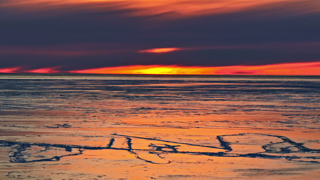 Aerial view of a frozen landscape at sunset with vibrant orange and red light reflecting on the ice in Latvia. Aerial view of a frozen landscape at sunset with vibrant orange and red light reflecting on the ice in Latvia.