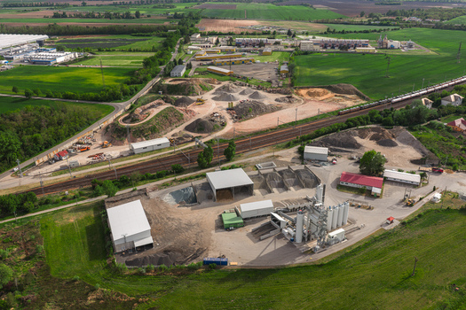 Aerial view of an industrial facility with gravel piles silos and a railway line passing through green fields in Hrusky South Moravian Region Czechia. Aerial view of an industrial facility with gravel piles silos and a railway line passing through green fields in Hrusky South Moravian Region Czechia.
