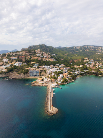 Aerial view of the stone breakwater with a lighthouse and hillside villas overlooking the turquoise Mediterranean waters in Port d Andratx Balearic Islands Spain. Aerial view of the stone breakwater with a lighthouse and hillside villas overlooking the turquoise Mediterranean waters in Port d Andratx Balearic Islands Spain.
