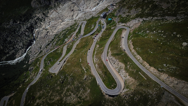 Aerial view of the winding Furka Pass road snaking through the steep rocky slopes and green alpine meadows of the Swiss Alps in Obergoms Valais Switzerland. Aerial view of the winding Furka Pass road snaking through the steep rocky slopes and green alpine meadows of the Swiss Alps in Obergoms Valais Switzerland.