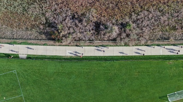 Aerial view of people walking and running along a paved path in a park with green grass and a soccer field in Boulder Colorado United States. Aerial view of people walking and running along a paved path in a park with green grass and a soccer field in Boulder Colorado United States.