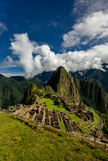 View of the Historic Sanctuary of Machu Picchu with ancient stone ruins lush green terraces and towering Andean mountains under a blue sky in Urubamba Province Cusco Peru.