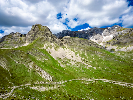 Aerial view of Bobotov Kuk with lush green mountain slopes rocky peaks and a winding road through the landscape in Zabljak Municipality Montenegro. Aerial view of Bobotov Kuk with lush green mountain slopes rocky peaks and a winding road through the landscape in Zabljak Municipality Montenegro.