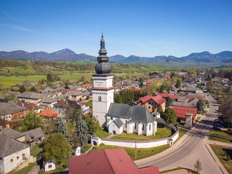 Aerial view of the historic St. Matthew s Church with its tall dark spire surrounded by village houses and green hills under a clear blue sky in Partizanska Lupca Zilina Region Slovakia. Aerial view of the historic St. Matthew s Church with its tall dark spire surrounded by village houses and green hills under a clear blue sky in Partizanska Lupca Zilina Region Slovakia.