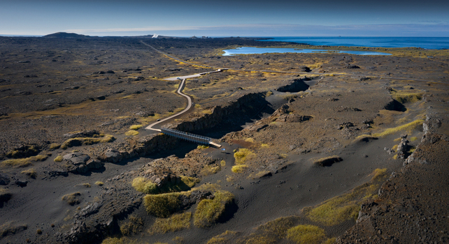 Aerial view of the Bridge Between Continents crossing a tectonic fissure in a vast volcanic landscape with dark lava fields and the ocean on the horizon Iceland.