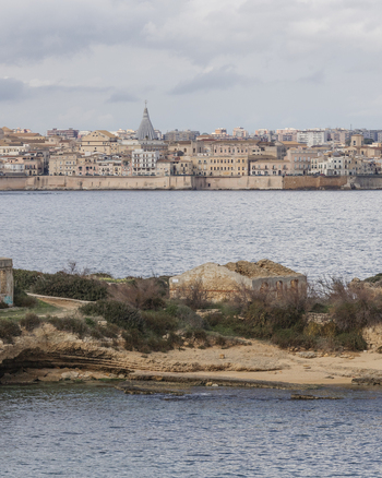 View of the historic Syracuse skyline and the Sanctuary of Our Lady of Tears across the blue water from a rocky coastline Syracuse Sicily Italy.