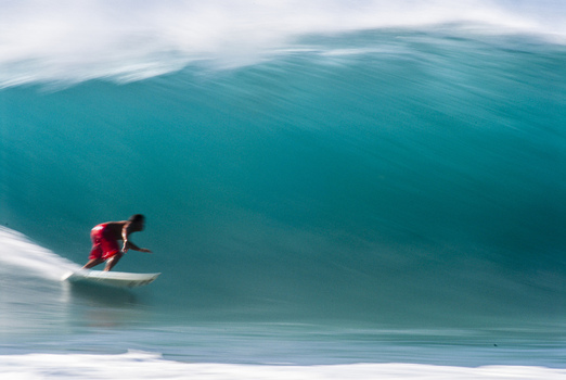 View of a surfer in red shorts riding a large powerful turquoise wave at the Banzai Pipeline in Haleiwa Hawaii United States.