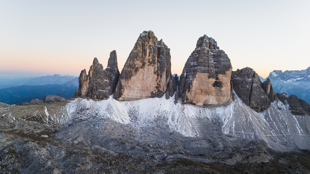 Aerial view of the iconic Tre Cime di Lavaredo peaks with a light dusting of snow on the rocky slopes under a soft twilight sky in Auronzo di Cadore Veneto Italy. Aerial view of the iconic Tre Cime di Lavaredo peaks with a light dusting of snow on the rocky slopes under a soft twilight sky in Auronzo di Cadore Veneto Italy.