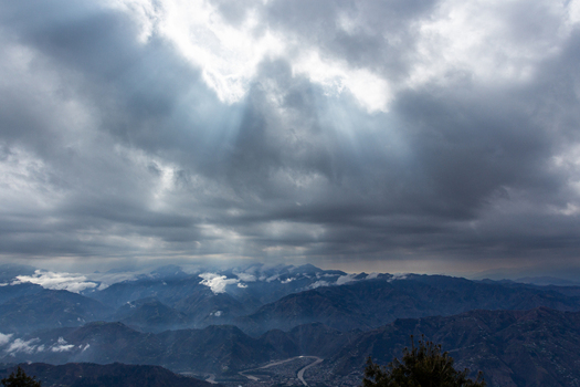 View of sunlight piercing through the dark ominous clouds blanketing the rugged mountain range and winding river below Muzaffarabad Azad Kashmir Pakistan. View of sunlight piercing through the dark ominous clouds blanketing the rugged mountain range and winding river below Muzaffarabad Azad Kashmir Pakistan.