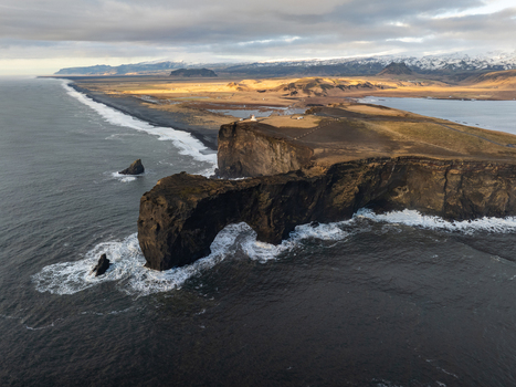 Aerial view of Dyrholaey arch with its iconic lighthouse dramatic black volcanic cliffs and crashing waves along the coastline in Myrdalshreppur Iceland. Aerial view of Dyrholaey arch with its iconic lighthouse dramatic black volcanic cliffs and crashing waves along the coastline in Myrdalshreppur Iceland.