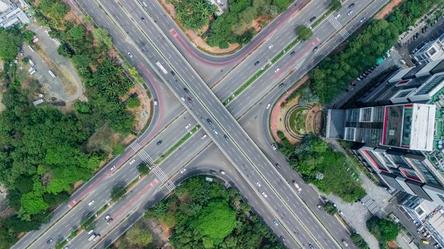 Aerial view of a complex highway interchange with multiple lanes and vehicles surrounded by lush green trees and modern urban architecture in Jakarta Indonesia. Aerial view of a complex highway interchange with multiple lanes and vehicles surrounded by lush green trees and modern urban architecture in Jakarta Indonesia.