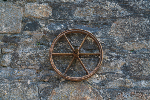 View of a rusty metal wheel mounted on a rough stone wall in Charlestown Cornwall United Kingdom. View of a rusty metal wheel mounted on a rough stone wall in Charlestown Cornwall United Kingdom.