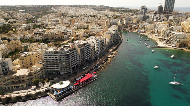 Aerial view of the urban waterfront of Spinola Bay with boats moored in the clear water and buildings lining the coast in Malta. Aerial view of the urban waterfront of Spinola Bay with boats moored in the clear water and buildings lining the coast in Malta.