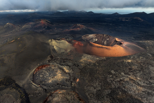 Aerial view of volcanic craters and dark lava fields under a dramatic cloudy sky in Lanzarote Canarias Spain. Aerial view of volcanic craters and dark lava fields under a dramatic cloudy sky in Lanzarote Canarias Spain.