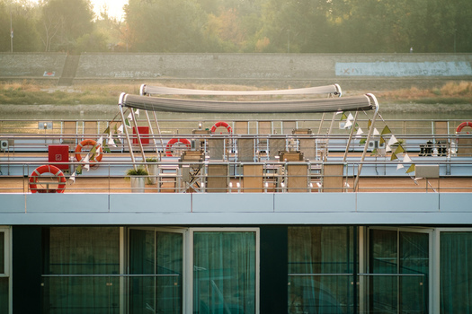 View of the sunlit deck of a river cruise ship with tables chairs and lifebuoys docked along the river in Novi Sad Vojvodina Serbia. View of the sunlit deck of a river cruise ship with tables chairs and lifebuoys docked along the river in Novi Sad Vojvodina Serbia.