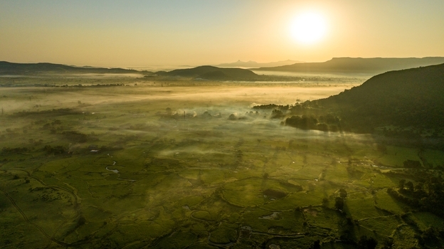 Aerial view of the misty landscape in Igatpuri at sunrise with rolling green hills and golden light illuminating the valley in Igatpuri Maharashtra India.