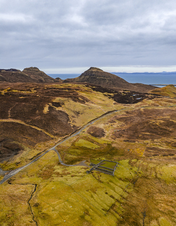 Aerial view of The Quiraing featuring the rugged mountain landscape winding road and stone structures under a cloudy sky Isle of Skye Scotland United Kingdom. Aerial view of The Quiraing featuring the rugged mountain landscape winding road and stone structures under a cloudy sky Isle of Skye Scotland United Kingdom.